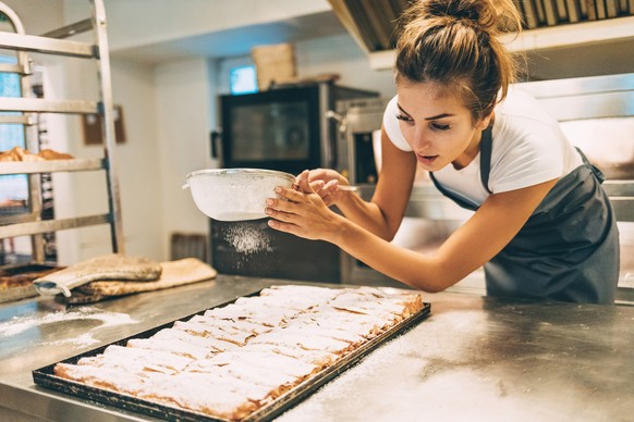 Smiling young baker dusting pastry with powdered sugar in a commercial kitchen