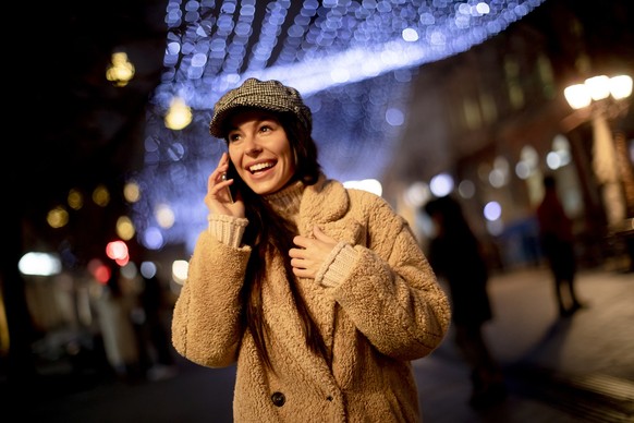 Beautiful young woman using her mobile phone in the street at Christmas time