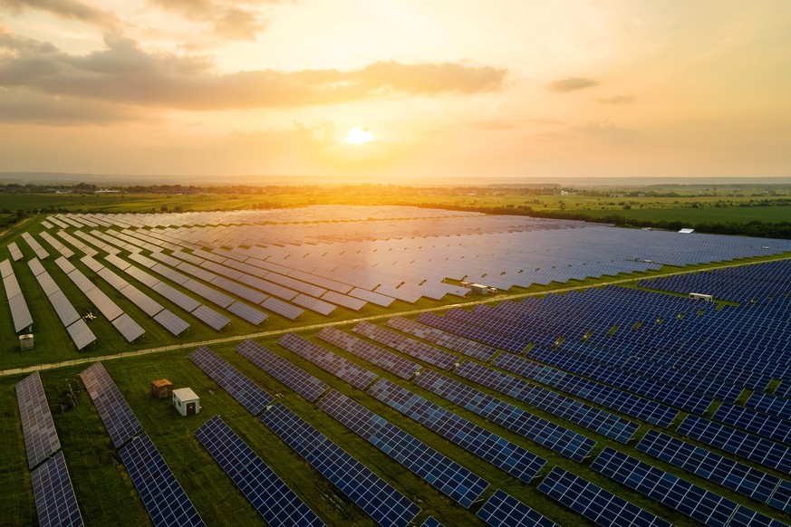Aerial view of large sustainable electrical power plant with many rows of solar photovoltaic panels for producing clean ecological electric energy in evening. Renewable electricity with zero emission  ...