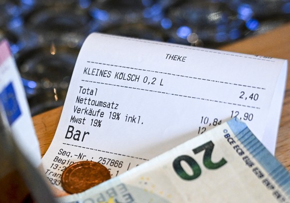 PRODUKTION - 05.01.2024, Berlin: Ein Kassenbon mit einer Mehrwertsteuer von 19 Prozent für Speisen und Getränke und Geldscheine liegen im Restaurant Ständige Vertretung. Größere Restaurants verzichten ...