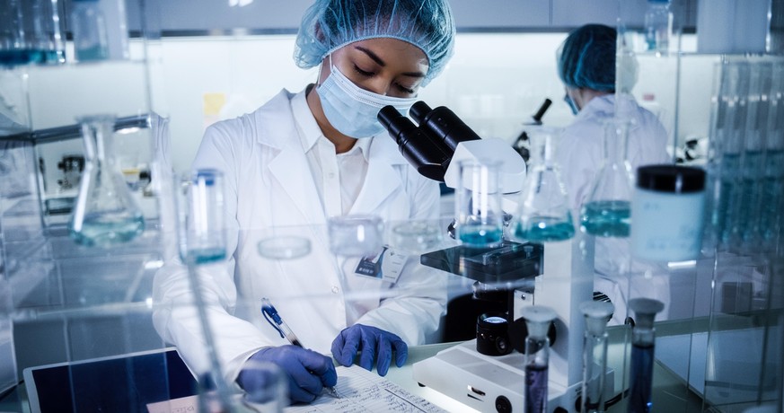 Scientists examines DNA models in modern Genetic Research Laboratory. Computer monitors with data in foreground