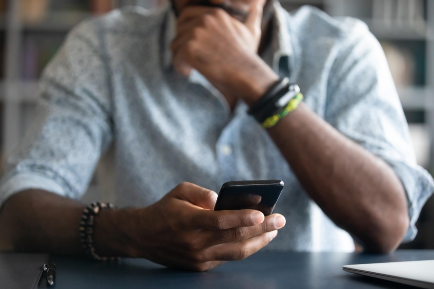 African guy holds cell phone close up view hands and device man feels concerned on background, received unpleasant sms, wait or missed important call, waste time online, addicted with internet concept