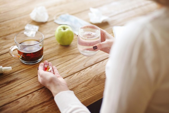 High angle of anonymous female with pills and cup of water witting at table with tea and apple during illness || Modellfreigabe vorhanden