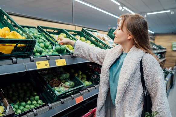 Smiling woman taking fresh organic limes in the supermarket store during selecting fresh products. Grocery Shopping. Healthy eating diet, go vegan. Veganuary month. Selective focus. Copy space Model R ...