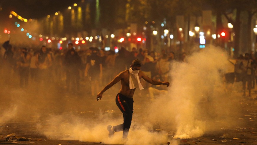 A man kicks a tear gas canister thrown by riot police during clashes on the Champs Champs Elysees avenue where soccer fans were celebrating France&#039;s World Cup victory over Croatia in Paris, Franc ...