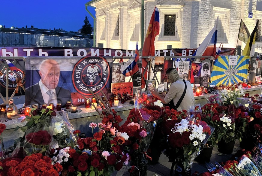 28.08.2023, Russland, Moskau: Ein junger Mann legt einen Gegenstand zwischen Blumen und Kerzen an die Gedenkst