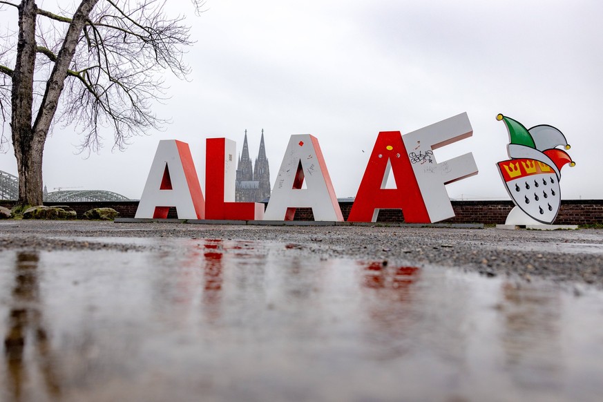Eine Skulptur mit dem Schriftzug ALAAF am Deutzer Rheinufer im Regen. Im Hintergrund der K