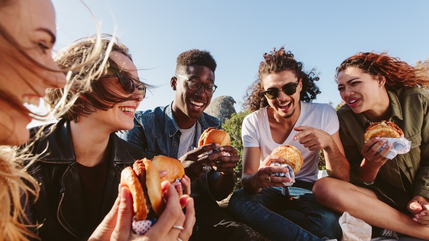 Young people having summer picnic and eating together sitting on mountain top. Happy friends on mountain top having a picnic on a summer day.