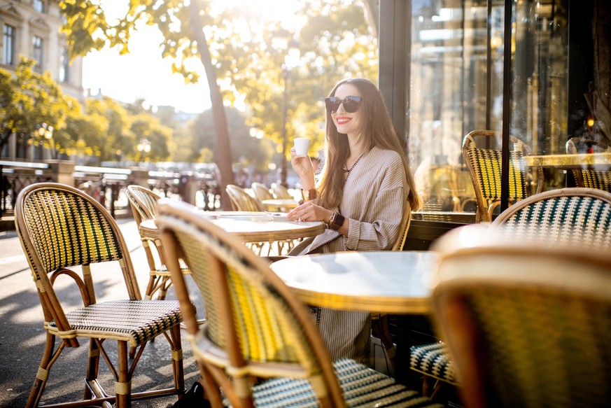 Portrait of a young woman enjoying coffee sitting outdoors at the traditional french cafe during the morning in Paris