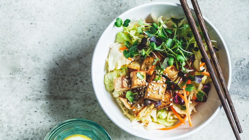 Fried tofu salad with sprouts and sesame seeds in a white bowl. Vegan food, asian food concept.