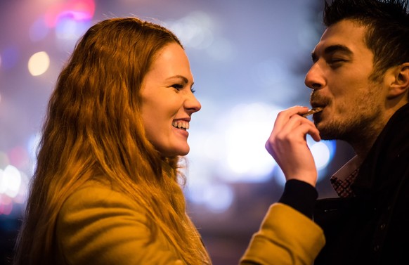 Couple on date - woman feeds her boyfriend with chocolate in street at winter night