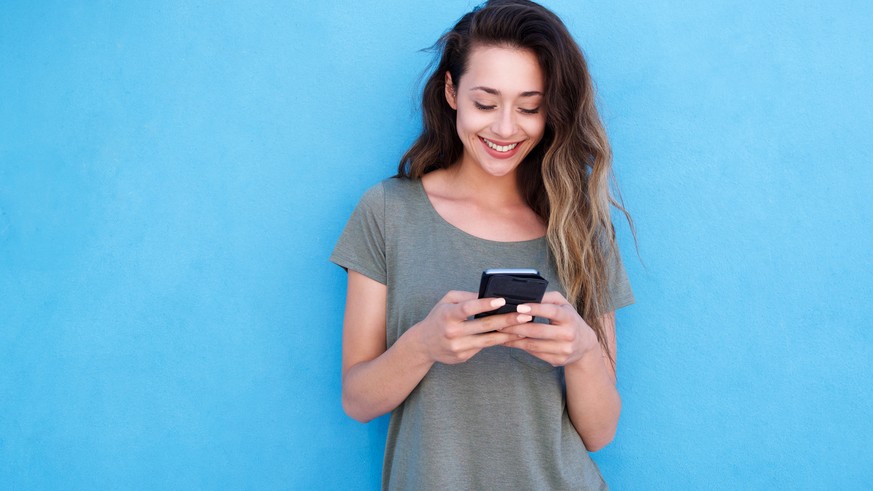 Front portrait of young smiling woman using mobile phone against blue background