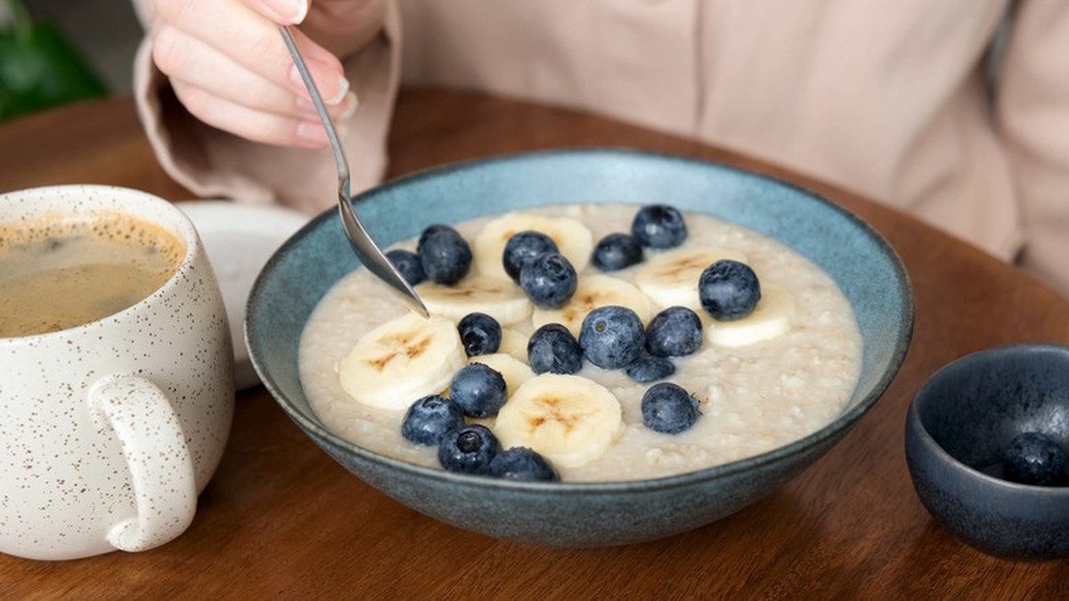 Healthy breakfast bowl of oatmeal porridge with blueberries and banana slices. Woman eating healthy breakfast