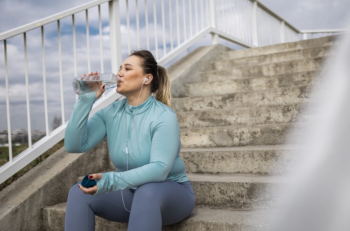 Overweight woman hydrating after exercise sitting on steps