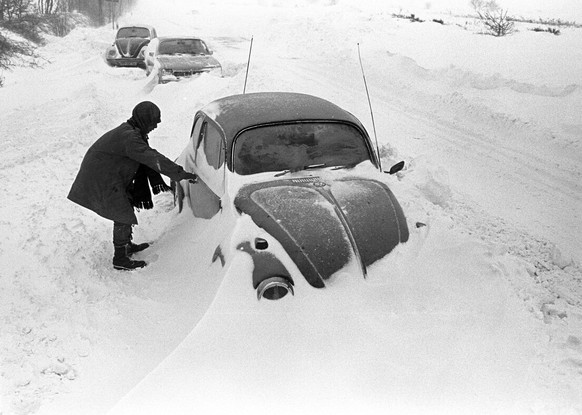 31.12.1978, Niedersachsen, Cuxhaven: Ein Autofahrer steht neben seinem am Straßenrand im Schnee stecken gebliebenen VW-Käfer.