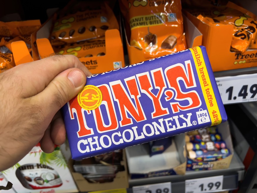 Dortmund, Germany - Feb 19, 2022: POV male hand holding package pack with Tony&#039;s Chocolonely toffee chocolate with shelves in supermarket in background xkwx milk, store, food, supermarket, shop,  ...