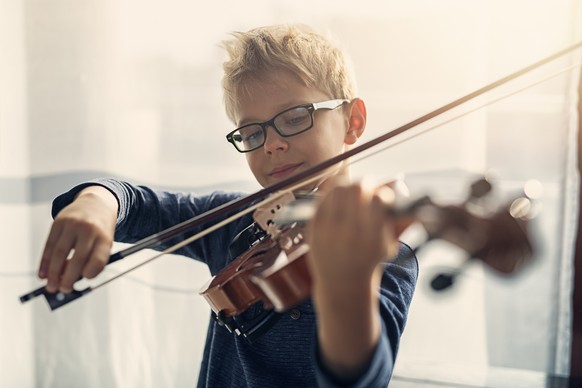 Closeup portrait of a focused little boy playing violin. The boy is aged 7 and is playing in a sunny room.