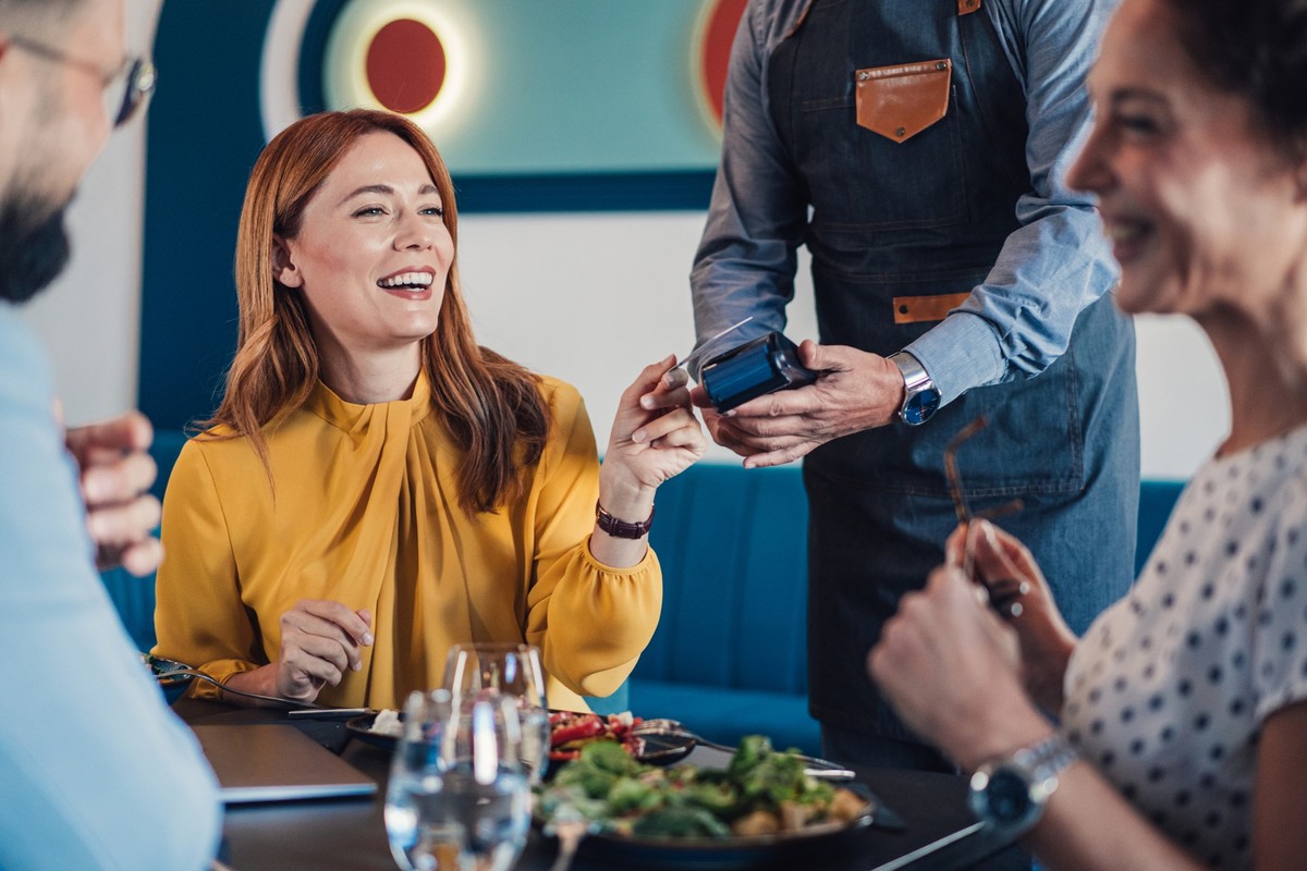Shot of a businesswoman paying for a lunch with business entrepreneurs. Group of businesspeople enjoying lunch at a restaurant, and businesswoman paying with a credit card via contactless payment. Bus ...