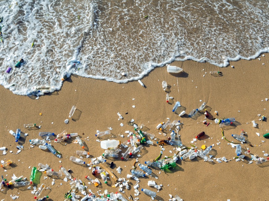 Plastic waste polluting the beach, mostly bottles that are pushed and attracted to the waves
