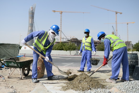 ARCHIV - 09.01.2016, Katar, Doha: Bauarbeiter aus Sri Lanka arbeiten auf einer Baustelle vor dem Hotel �The Torch� (l) und dem Khalifa International Stadium. (zu dpa: �WM-Pr�mien f�r Arbeitsmigranten  ...