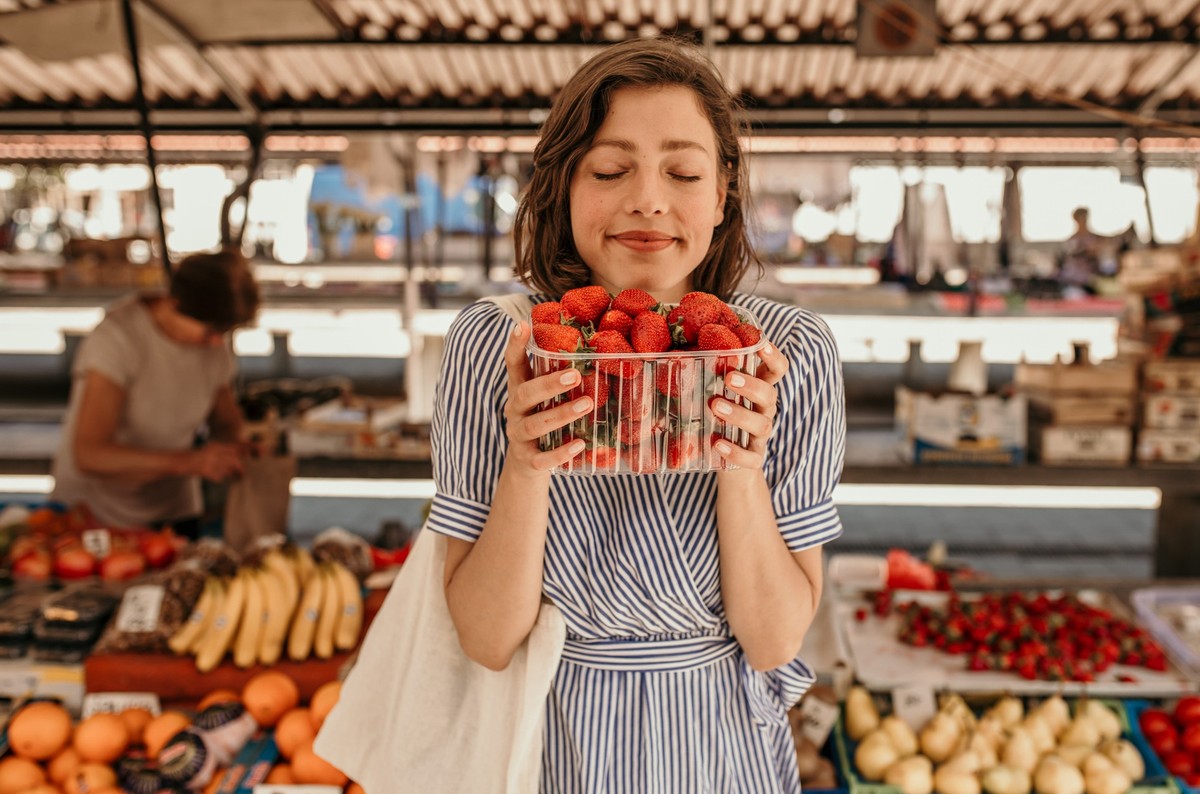 Portrait of a satisfied brunette holding fresh fruits just bought from an old lady market vendor.