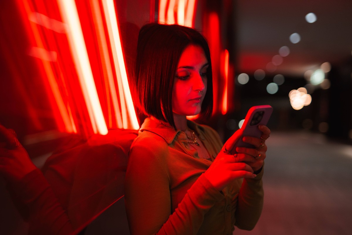 A young woman engrossed in her smartphone under vibrant neon lights, with an urban backdrop depicting the modern lifestyle in Madrid s Four Towers Business Area. Model Released PabloMenendez_ID19677_5 ...