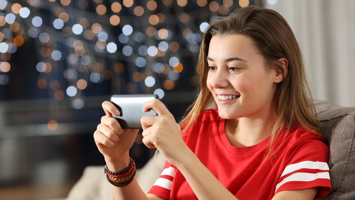 Teen watching media in a smart phone in the night sitting on a couch in the living room at home