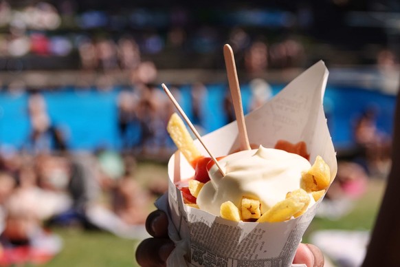 20.07.2022, Hamburg: Ein Badegast h�lt eine Portion Pommes Frites mit Ketchup und Mayonnaise im Kaifu-Freibad. Nach der Hitze im Westen Deutschlands schwitzt nun der Osten. Am Mittwoch w�rden �rtlich  ...