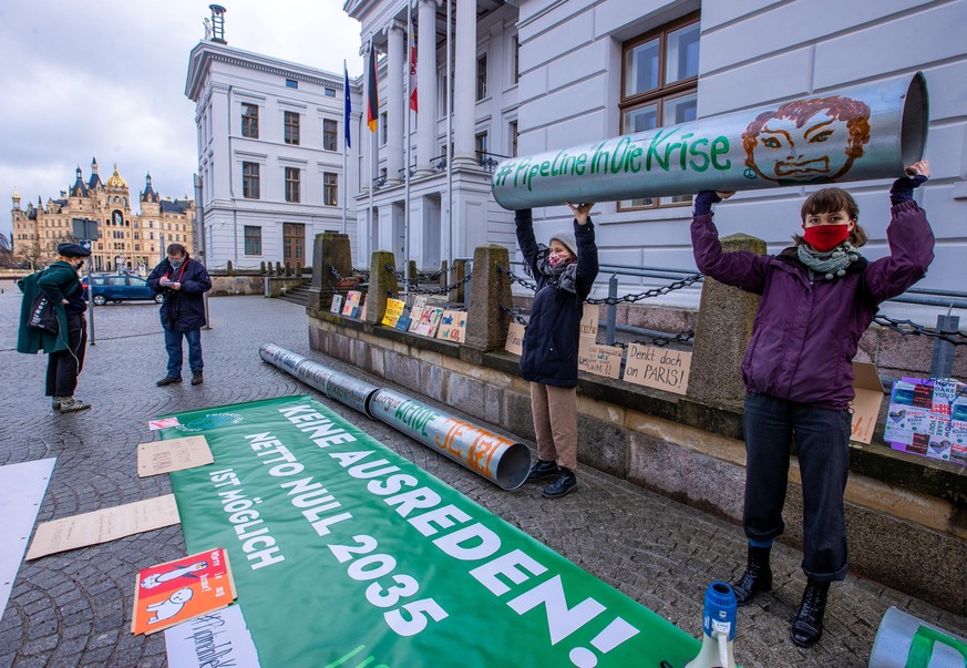 12.01.2021, Mecklenburg-Vorpommern, Schwerin: Mitglieder von &quot;Fridays for Future&quot; protestieren mit einer symbolischen Rohrleitung vor der Staatskanzlei gegen den Weiterbau der Gaspipeline No ...