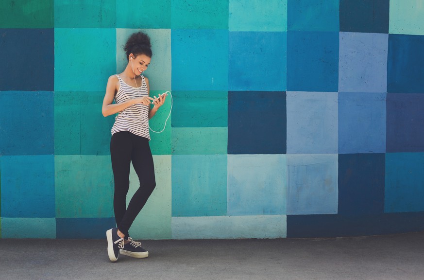 Happy smiling african-american woman leaning on bright blue graffiti wall, while listening music, relaxing from jog training, copy space