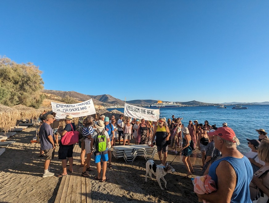 HANDOUT - 02.08.2023, Griechenland, -: Menschen demonstrieren mit Bannern mit der Aufschrift &quot;Reclaim the beach&quot; an einem Strand auf der Kykladen-Insel Paros. Ein paar Dutzend Bürger der Ins ...