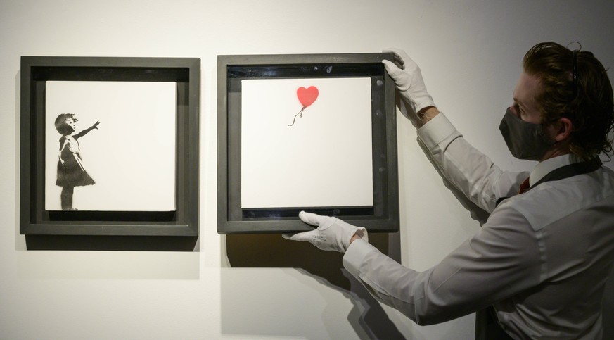 Entertainment Bilder des Tages Christies art handlers hold the iconic Banksy Diptych Girl and Balloon artwork at the preview of the 20th/21st Century Evening Sale which will be livestreamed across sal ...