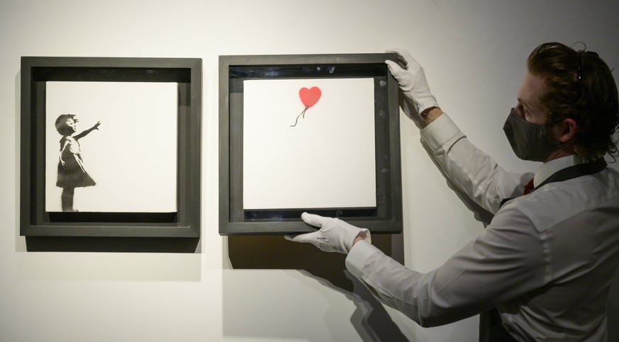 Entertainment Bilder des Tages Christies art handlers hold the iconic Banksy Diptych Girl and Balloon artwork at the preview of the 20th/21st Century Evening Sale which will be livestreamed across sal ...