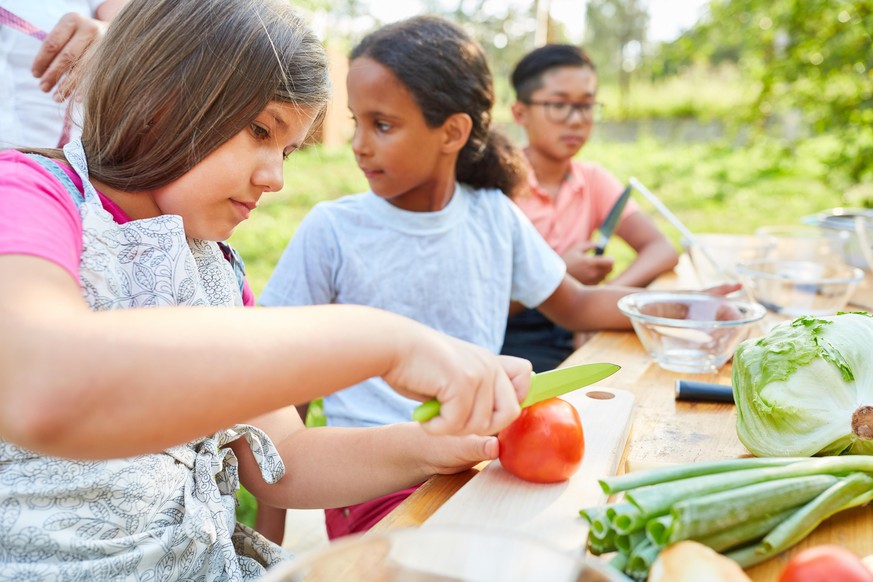 Kinder bei Kochkurs im Ferienlager bereiten Salat zu und lernen über gesunde Ernährung