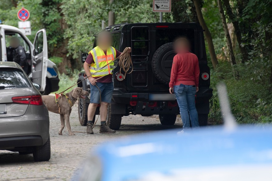 20.07.2023, Brandenburg, Kleinmachnow: Zwei Männer, davon einer mit Hund und einer Weste mit Aufschrift &quot;Gemeindejäger&quot; stehen bei einer Suchaktion nach einem freilaufenden gefährlichen Wild ...