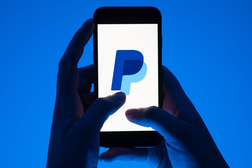 ARCHIV - 12.05.2022, Sachsen, Dresden: ILLUSTRATION - Eine Frau hält ein Smartphone mit dem Logo des Bezahldienst Paypal. (gestellte Szene) Paypal gibt am 03.11.2022 Zahlen für das 3. Quartal bekannt. ...