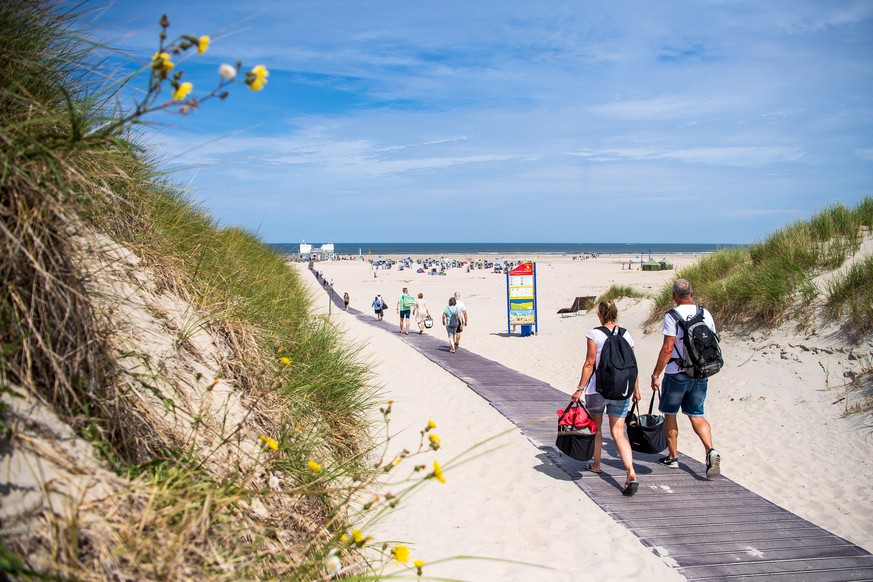 18.07.2022, Niedersachsen, Norderney: Touristen gehen am Strand der ostfriesischen Insel Norderney entlang. Foto: Sina Schuldt/dpa +++ dpa-Bildfunk +++