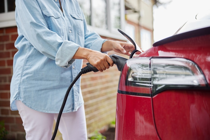 Close Up Of Woman Attaching Charging Cable To Environmentally Friendly Zero Emission Electric Car At Home