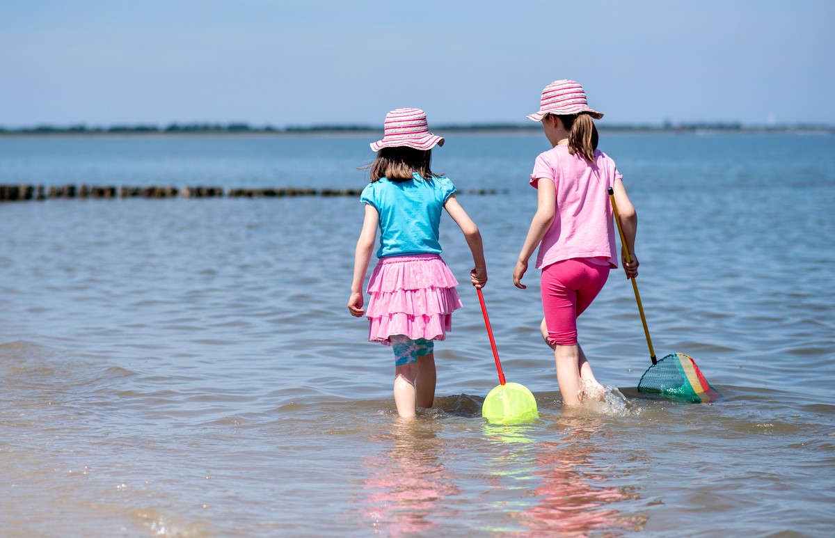 15.06.2022, Niedersachsen, Hooksiel: Zwei M�dchen spielen bei sonnigem Wetter mit ihren Keschern im flachen Wasser der Nordsee am Strand. In Wilhelmshaven findet der Nordsee-Tourismustag 2022 statt. I ...