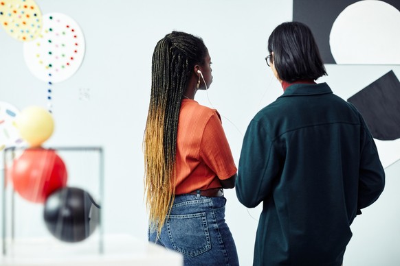 Rear view of ethnically diverse young man and woman looking at abstract painting and listening to audio tour at exhibition in art gallery Bei Regen Museum Date zu zweit schlechtes Wetter Mann Frau Kun ...