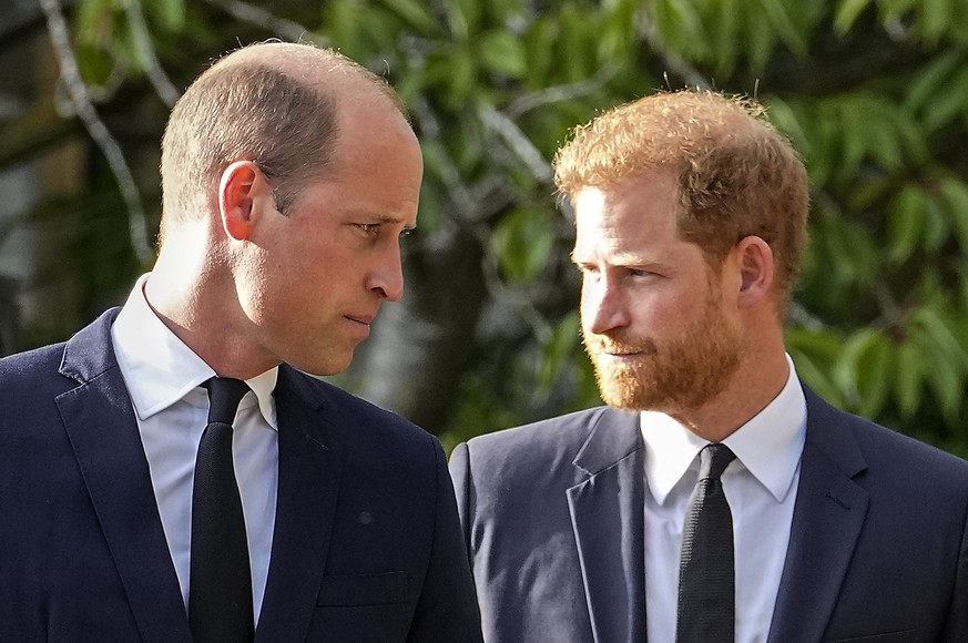 ARCHIV - 10.09.2022, Großbritannien, Windsor: Prinz William (l) und sein Bruder Prinz Harry gehen nebeneinander, nachdem sie die Blumengrüße für ihre verstorbene Großmutter vor Schloss Windsor besicht ...