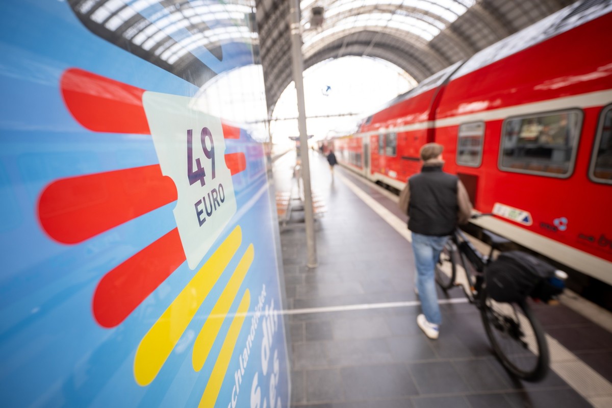 ARCHIV - 01.05.2023, Hessen, Frankfurt/Main: Ein Mann geht am Hauptbahnhof mit seinem Fahrrad zwischen der Werbung f�r das Deutschlandticket und einer Regionalbahn entlang. (Zu dpa �Deutschlandticketi ...