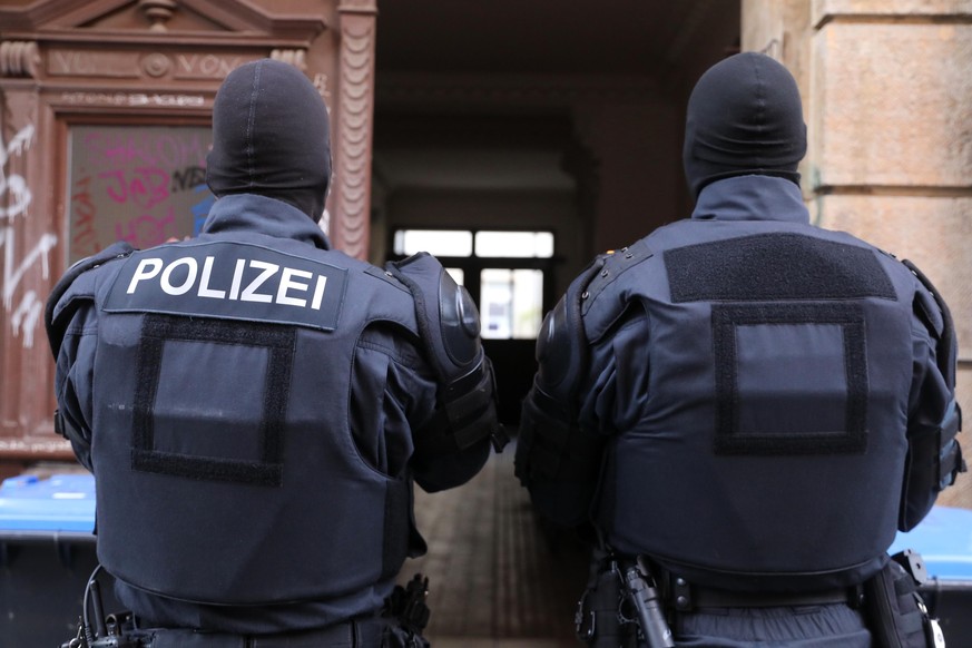 Zwei Polizisten stehen vor einem Hauseingang.Im Zusammenhang mit Krawallen im vorigen Mai hat die sächsische Polizei seit dem frühen Mittwochmorgen Wohnungen in Dresden, Görlitz, Zwickau und Chemnitz  ...