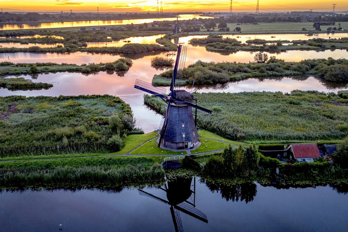 14.08.2023, Niederlande, Kinderdijk: Die Sonne geht hinter einer Windmühle auf. Etwa ein Drittel des Landes liegt unter dem Meeresspiegel, und Windmühlen verhindern, dass Regionen überflutet werden. F ...