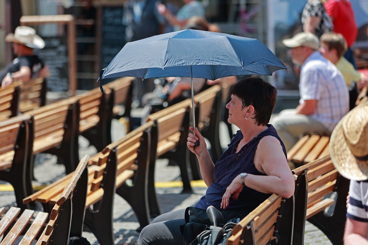 ARCHIV - 18.06.2023, NA, Wernigerode: Mit einem Schirm sitzt eine Frau in Wernigerode auf einer Bank. (zu dpa: «Wetterdienst warnt vor Hitze in Sachsen-Anhalt») Foto: Matthias Bein/dpa +++ dpa-Bildfun ...
