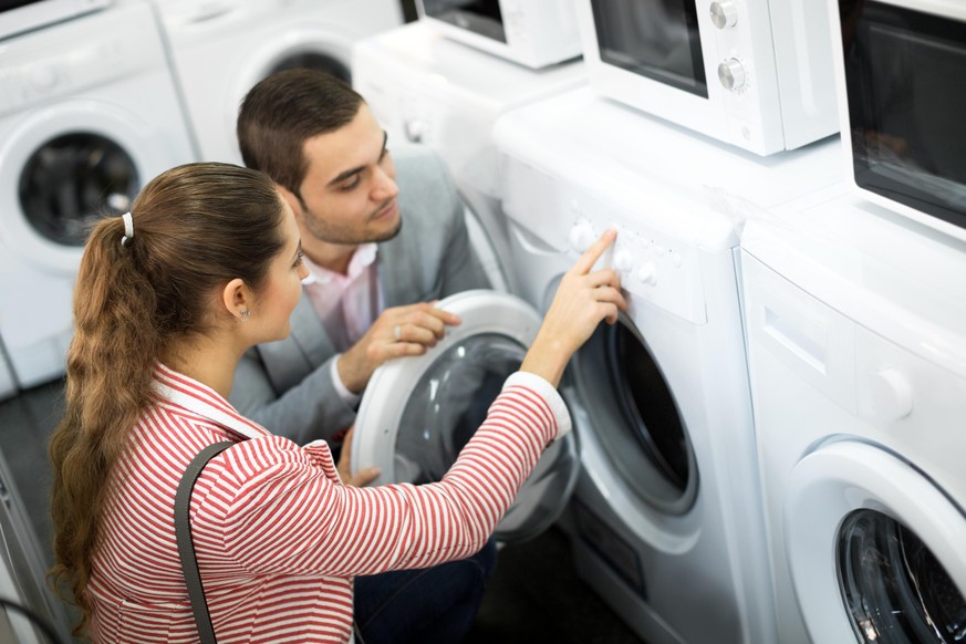 Cheerful young family couple buying new clothes washer in supermarket. Focus on the woman