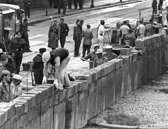 ARCHIV - 18.08.1961, DDR, Berlin: Unter der Aufsicht von bewaffneten Volkspolizisten errichtet eine Ostberliner Maurerkolonne am an der sowjetisch-amerikanischen Sektorengenze am Potsdamer Platz eine  ...