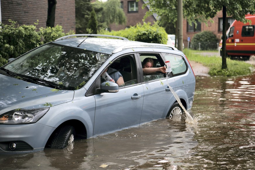Fahrzeuginsassen kippen eingelaufenes Wasser aus ihrem Auto zurück auf die überflutete Straße