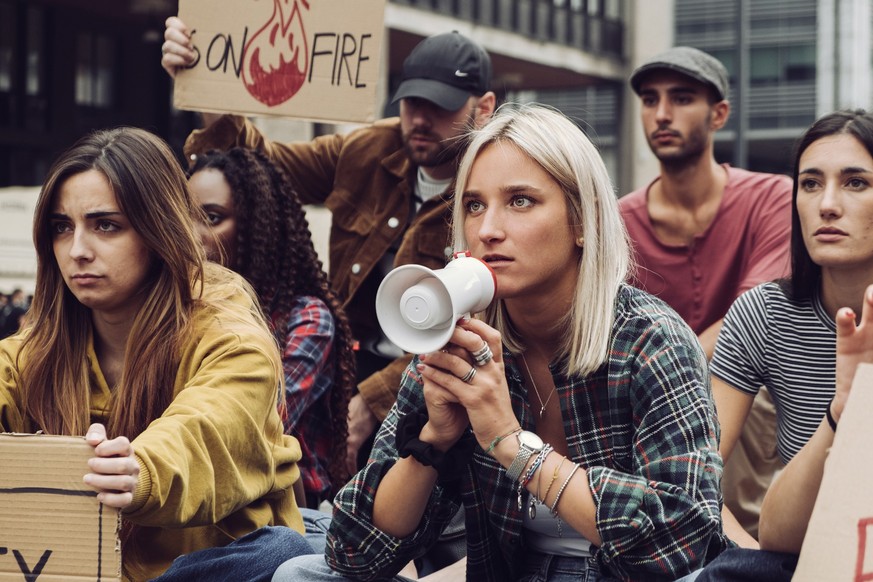 young protester sit-in - group of generation z people protesting against global warming holding megaphone and placards - people lifestyle concept