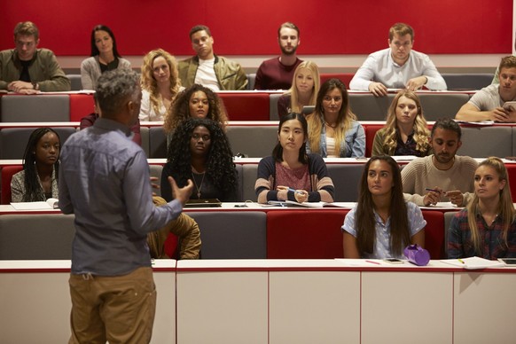 Achteraanzicht van een man die een presentatie geeft aan studenten in een collegezaal